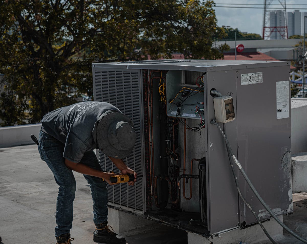HVAC technician working on air conditioning unit with drill